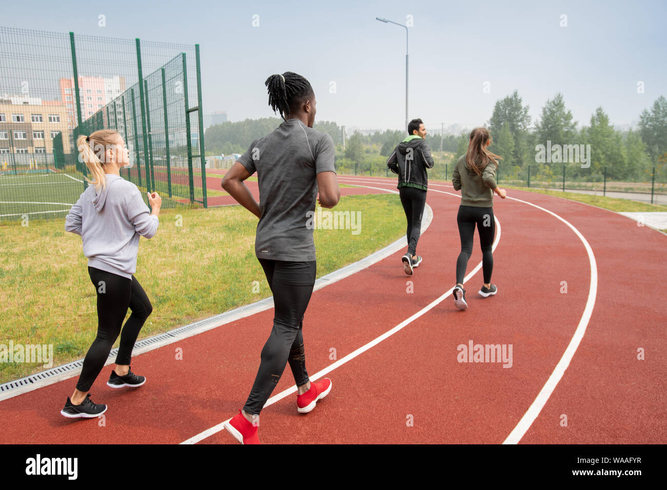 Rear view of young intercultural people in activewear running down race track Stock Photo