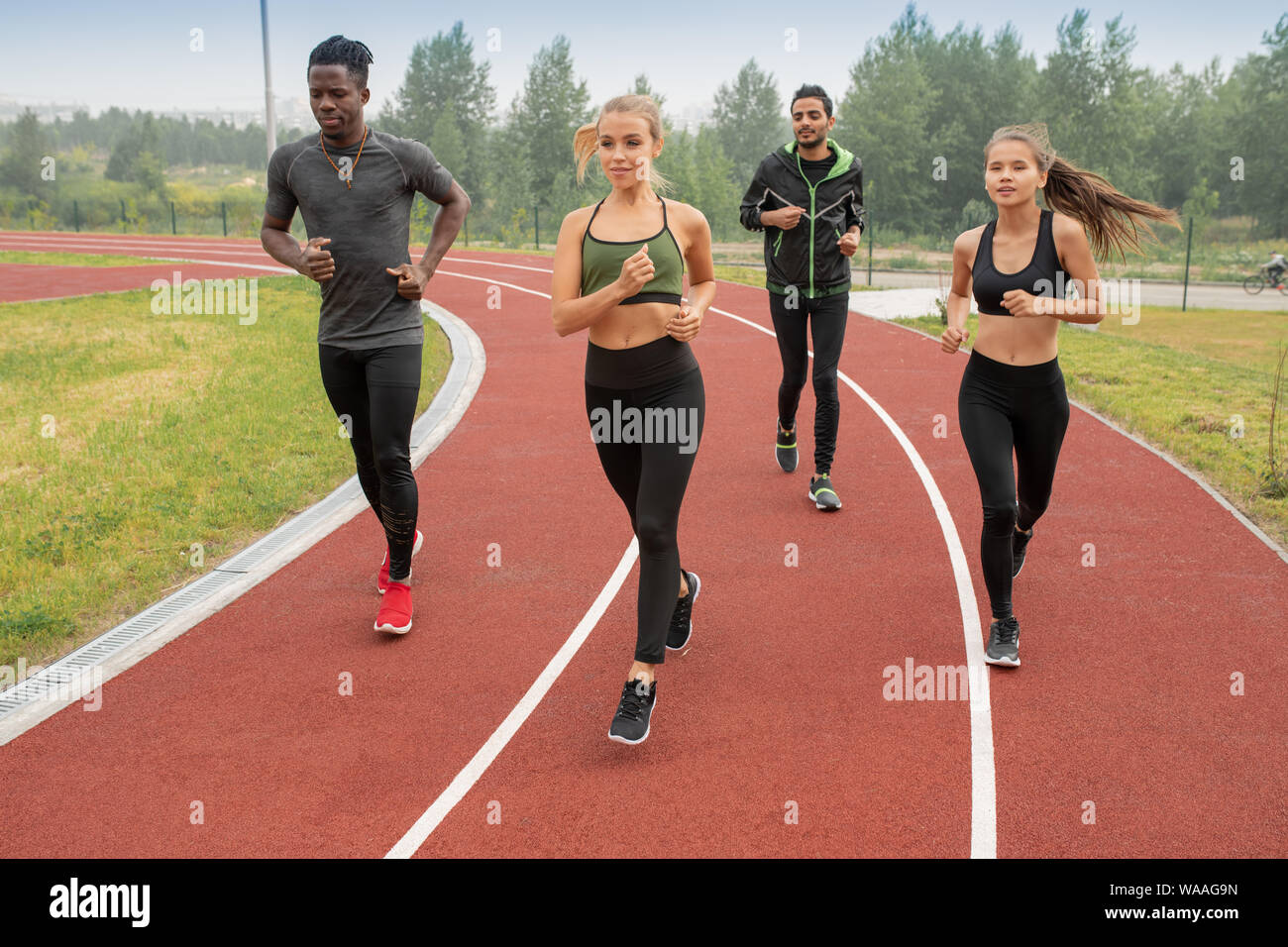 Group of active guys and girls in sportswear running down racetracks on stadium Stock Photo