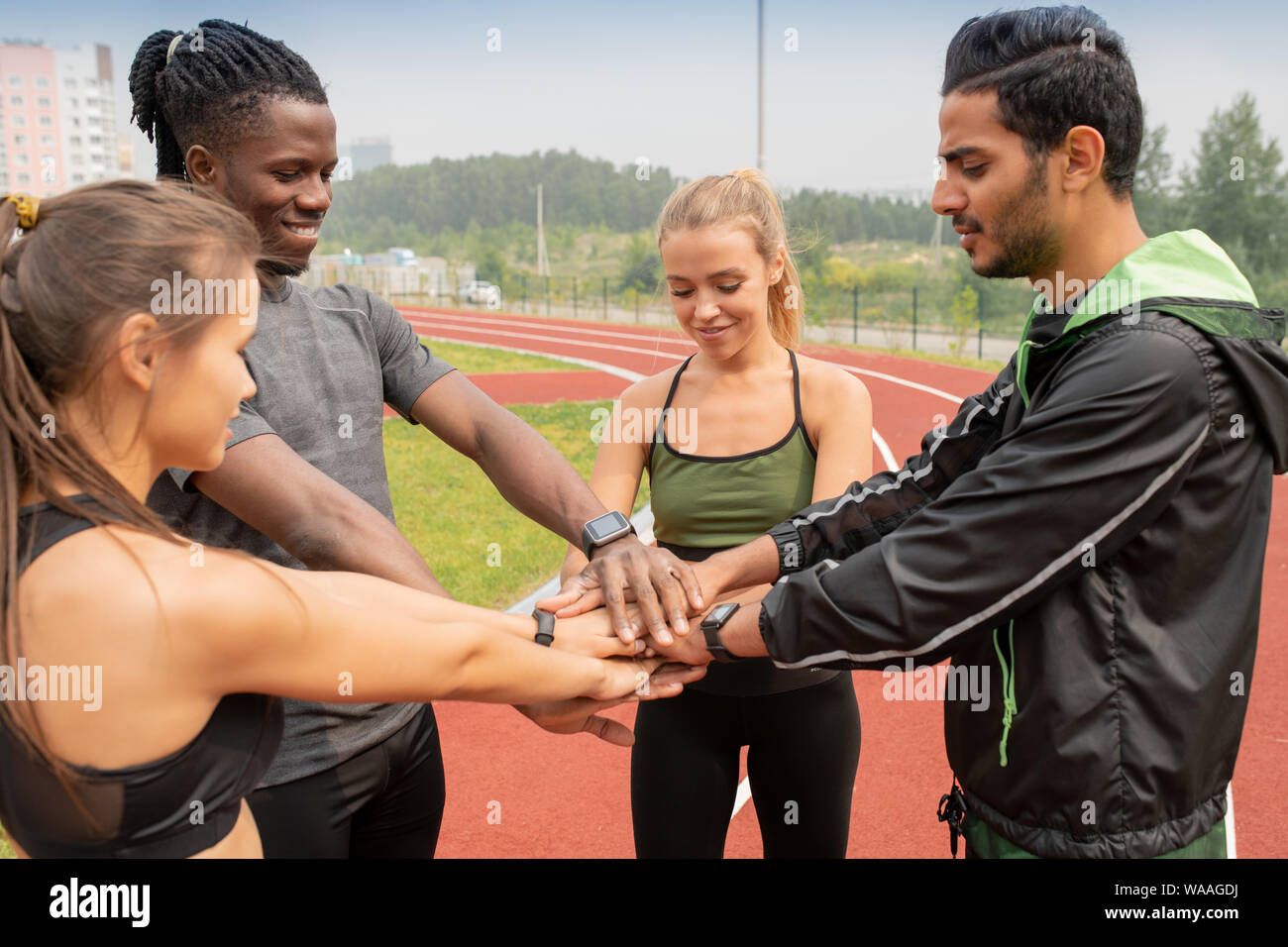 Four young intercultural people in activewear making pile of hands outdoors Stock Photo