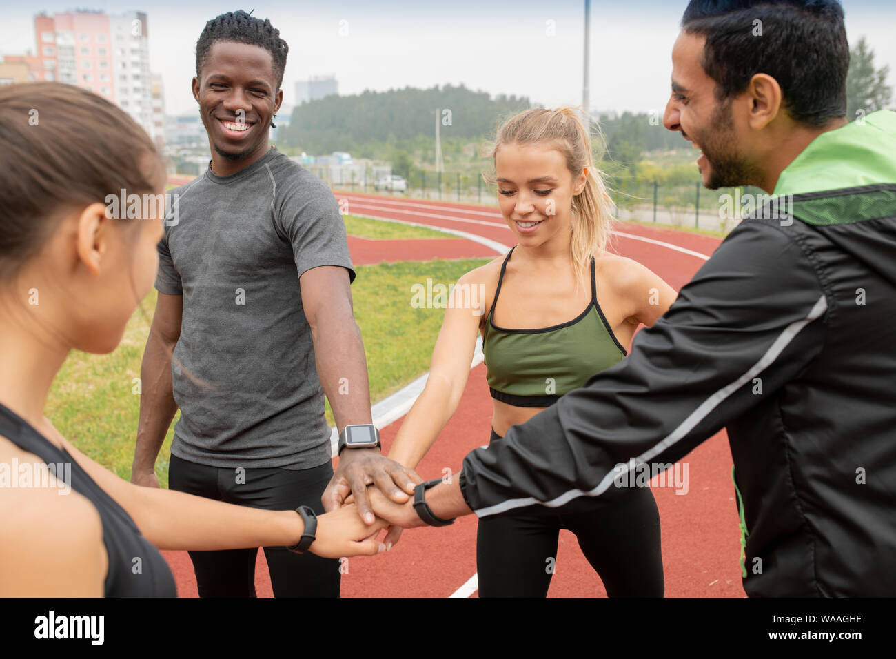 Four happy young athletes making pile of hands while standing on