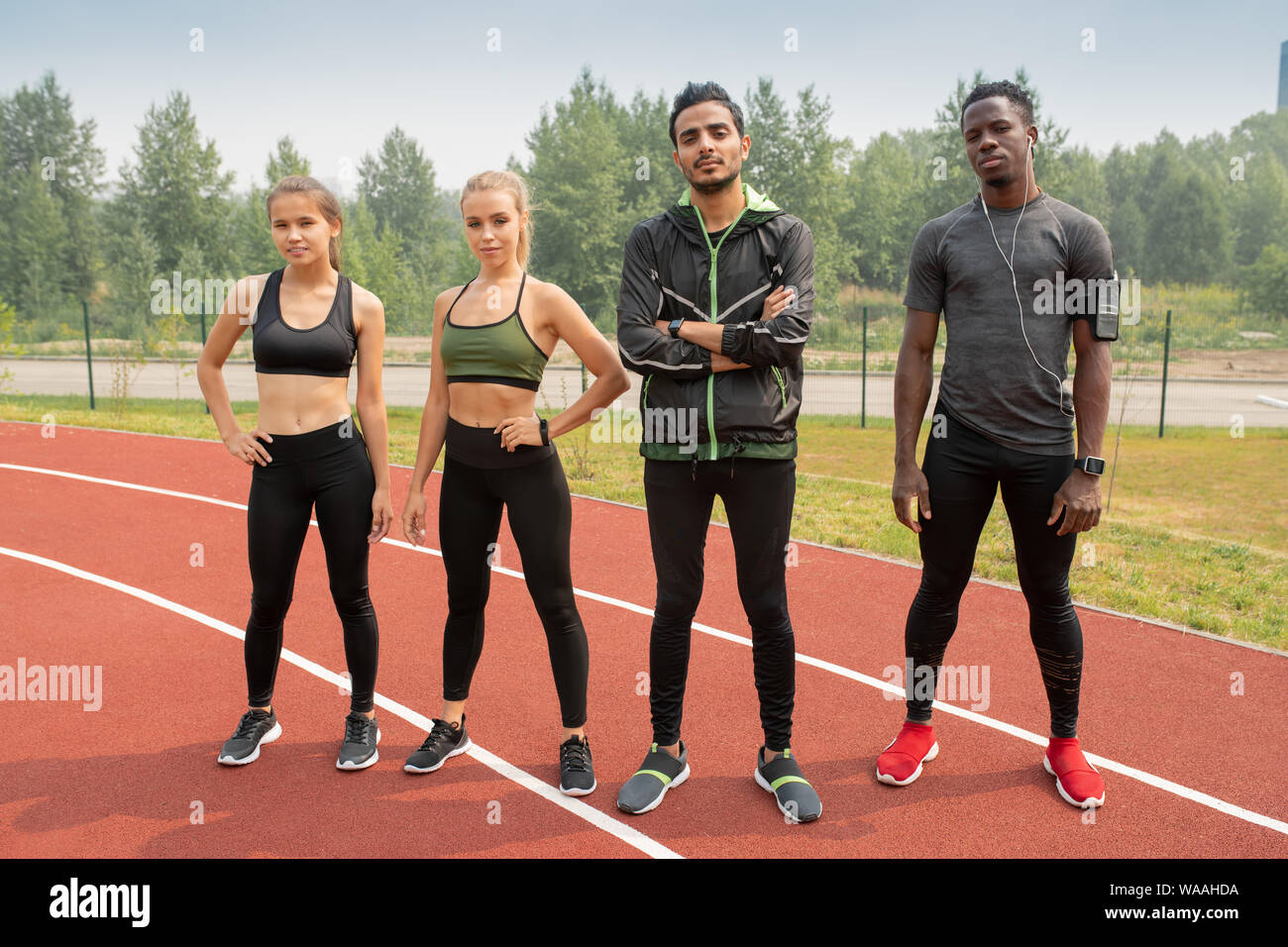 Row of young intercultural athletes in sportswear standing on racetracks Stock Photo