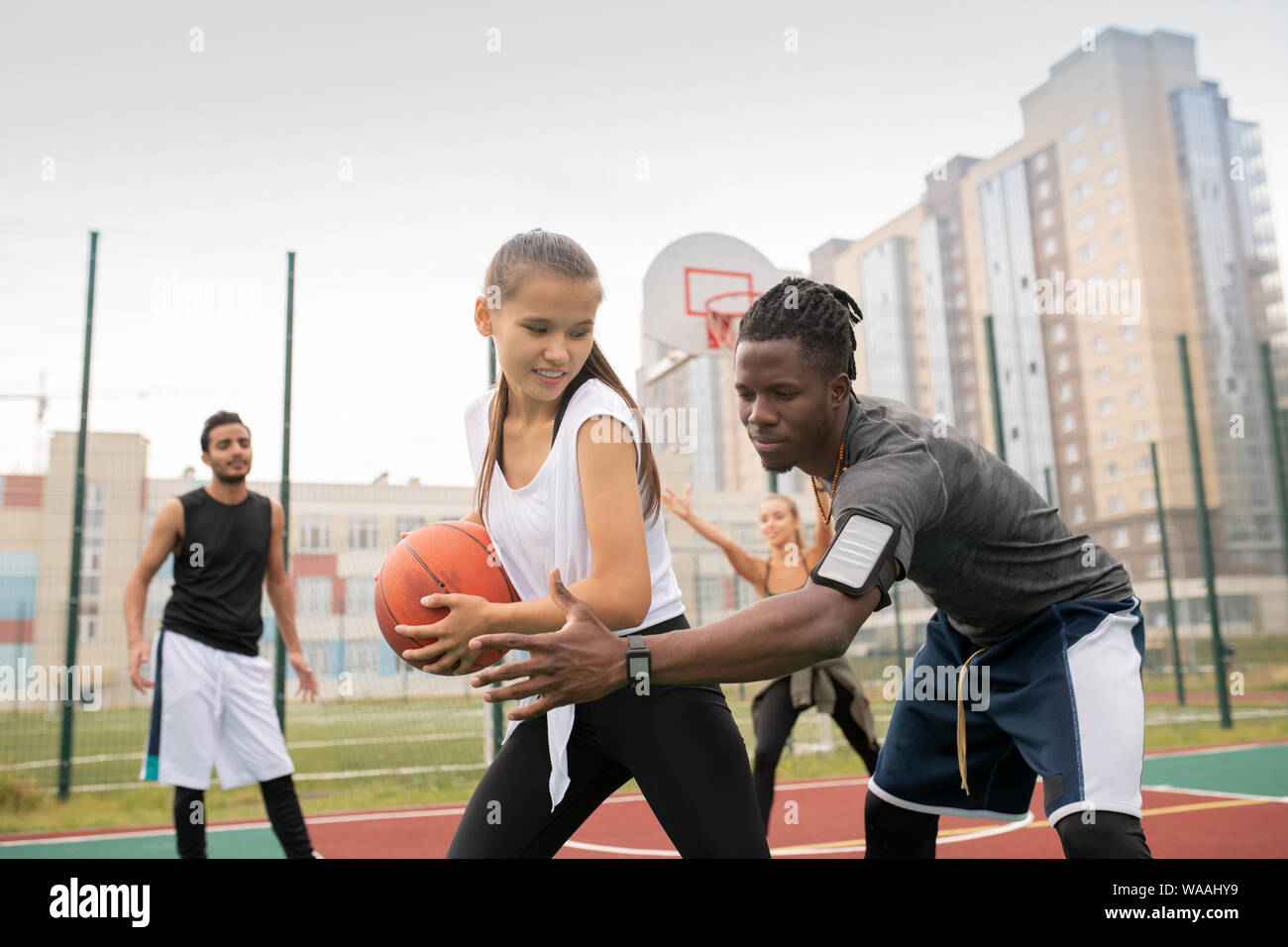 African basketballer keeping his hand by ball held by female player Stock Photo