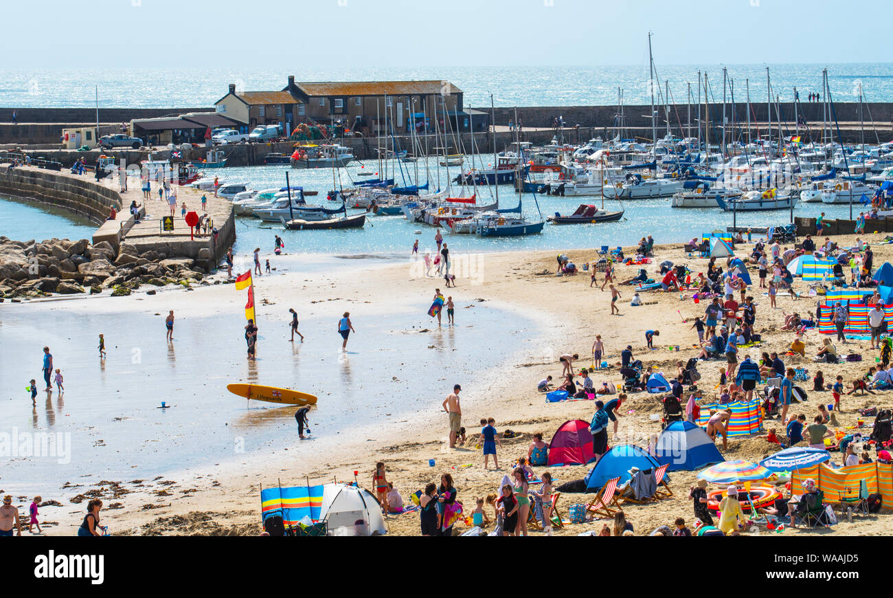 Lyme Regis, Dorset, UK. 19th Aug, 2019. UK Weather: Beachgoers and holidaymakers crowd the sandy beach at the pictureseque resort of Lyme Regis as summer sunshine returns after a weekend of heavy rain and high winds. Plenty of hot sun and blue skies are forecast in the run up to the August Bank Holiday weekend. Credit: Celia McMahon/Alamy Live News Stock Photo
