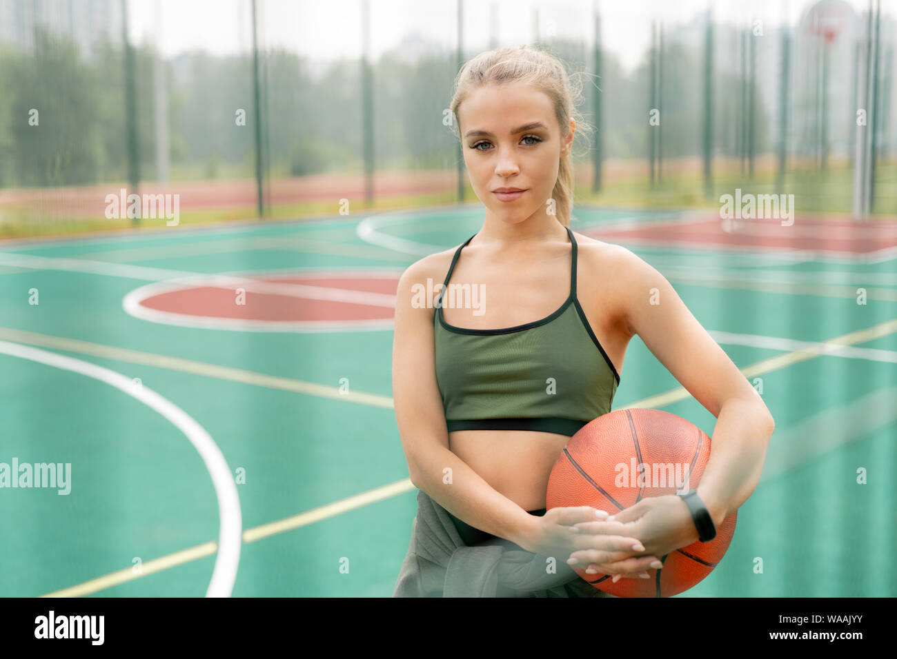 Pretty young woman in activewear holding ball for playing basketball Stock Photo