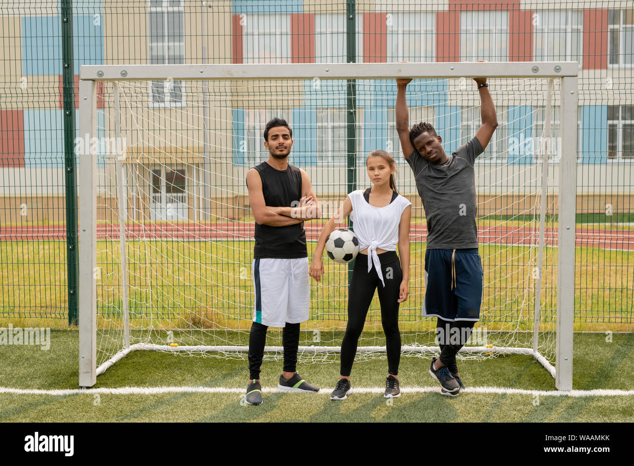 Three young soccer players in sportswear standing by gate on the field Stock Photo