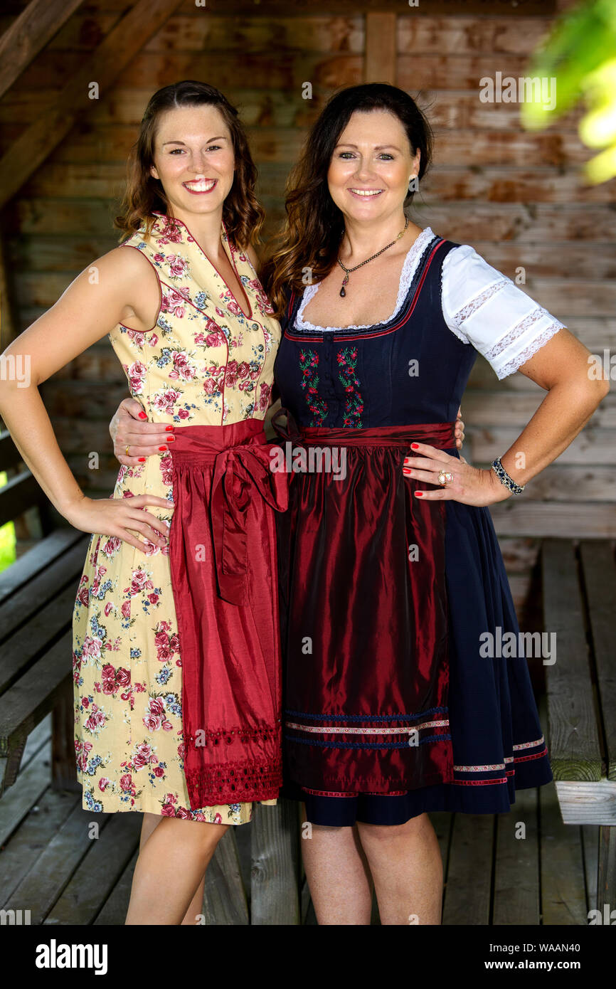 portrait of two bavarian women in dirndl standing by a wooden hut Stock Photo