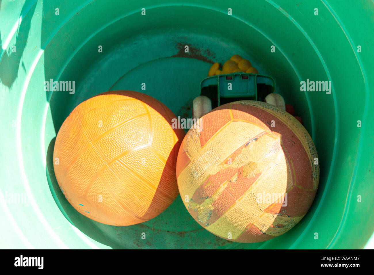 A close up view of rugby, soccor balls in a orange plastic bucket Stock Photo