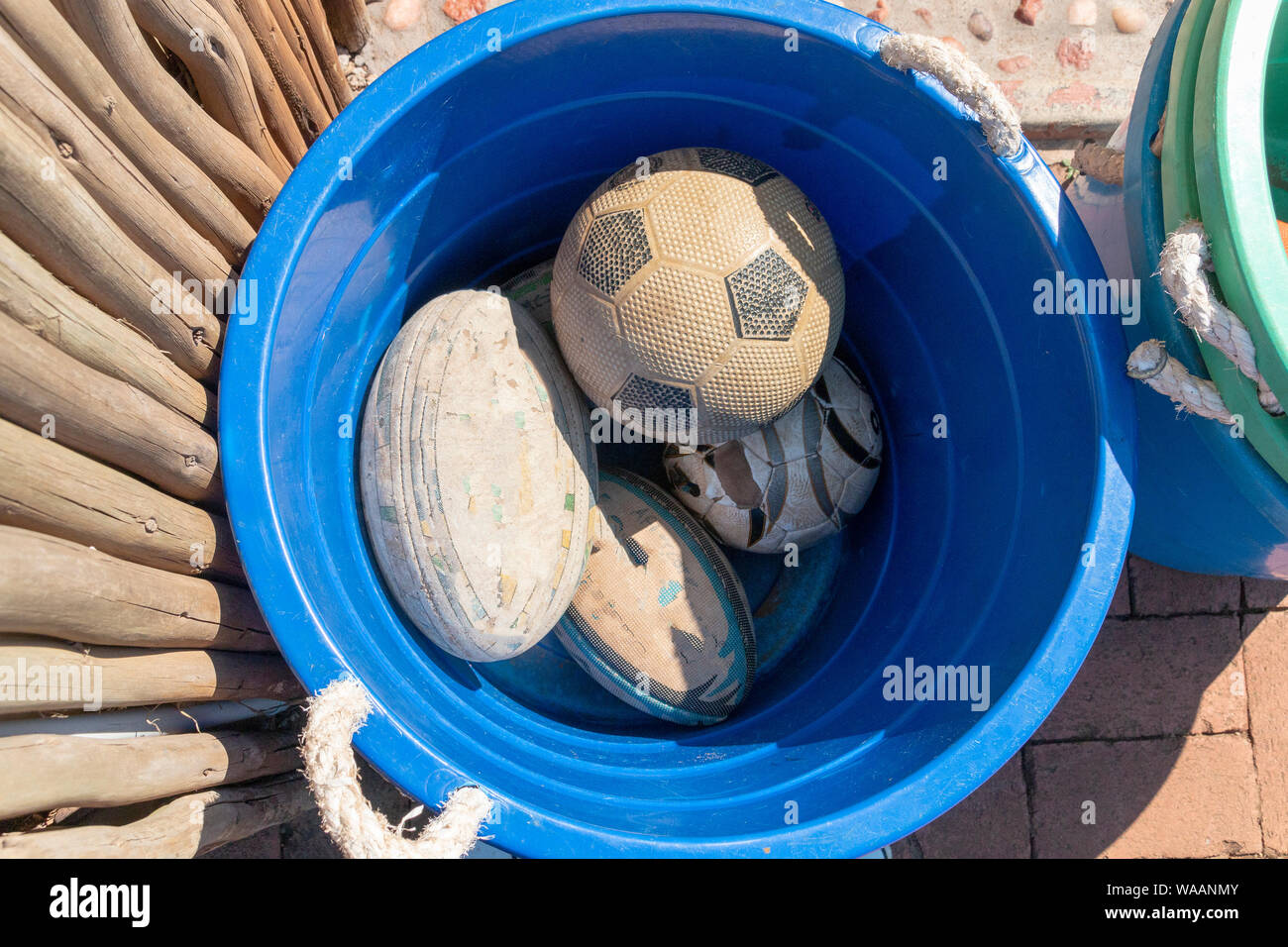 A close up view of rugby, soccor balls in a blue plastic bucket Stock Photo