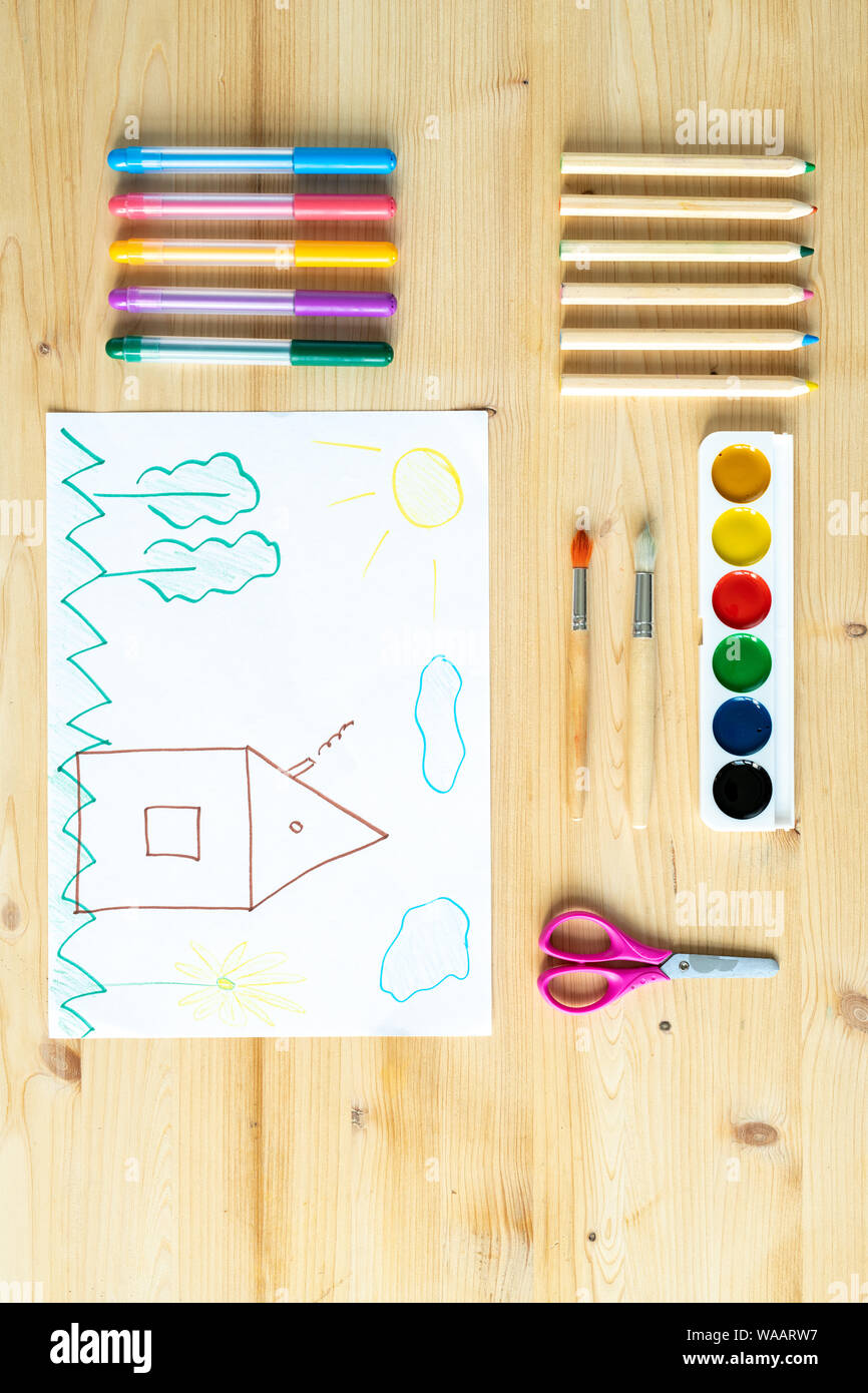 Child drawing on sheet of paper surrounded by supplies for drawing Stock Photo