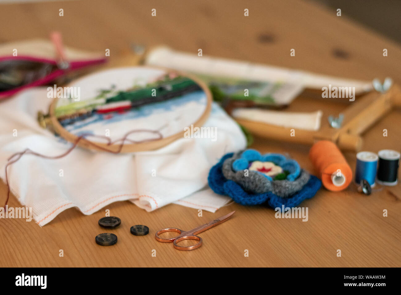 Cross-stitch embroidery materials, including threads, needles, scissors, linen and hoops. laid out on a table for craft/hobby Stock Photo