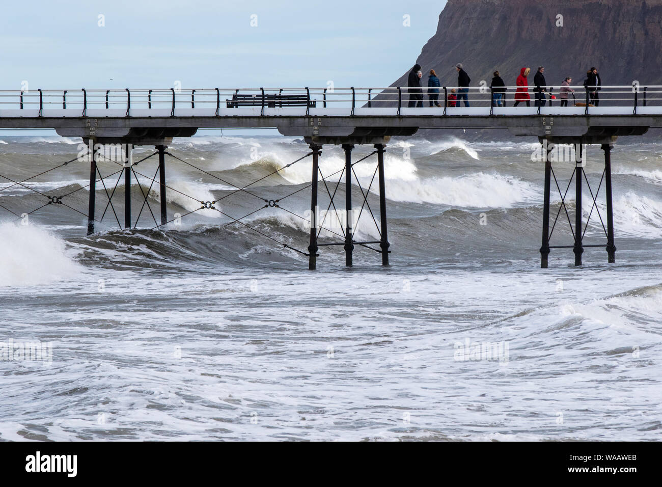 People walking on Saltburn pier during cold, stormy weather, with a strong surf below. Stock Photo