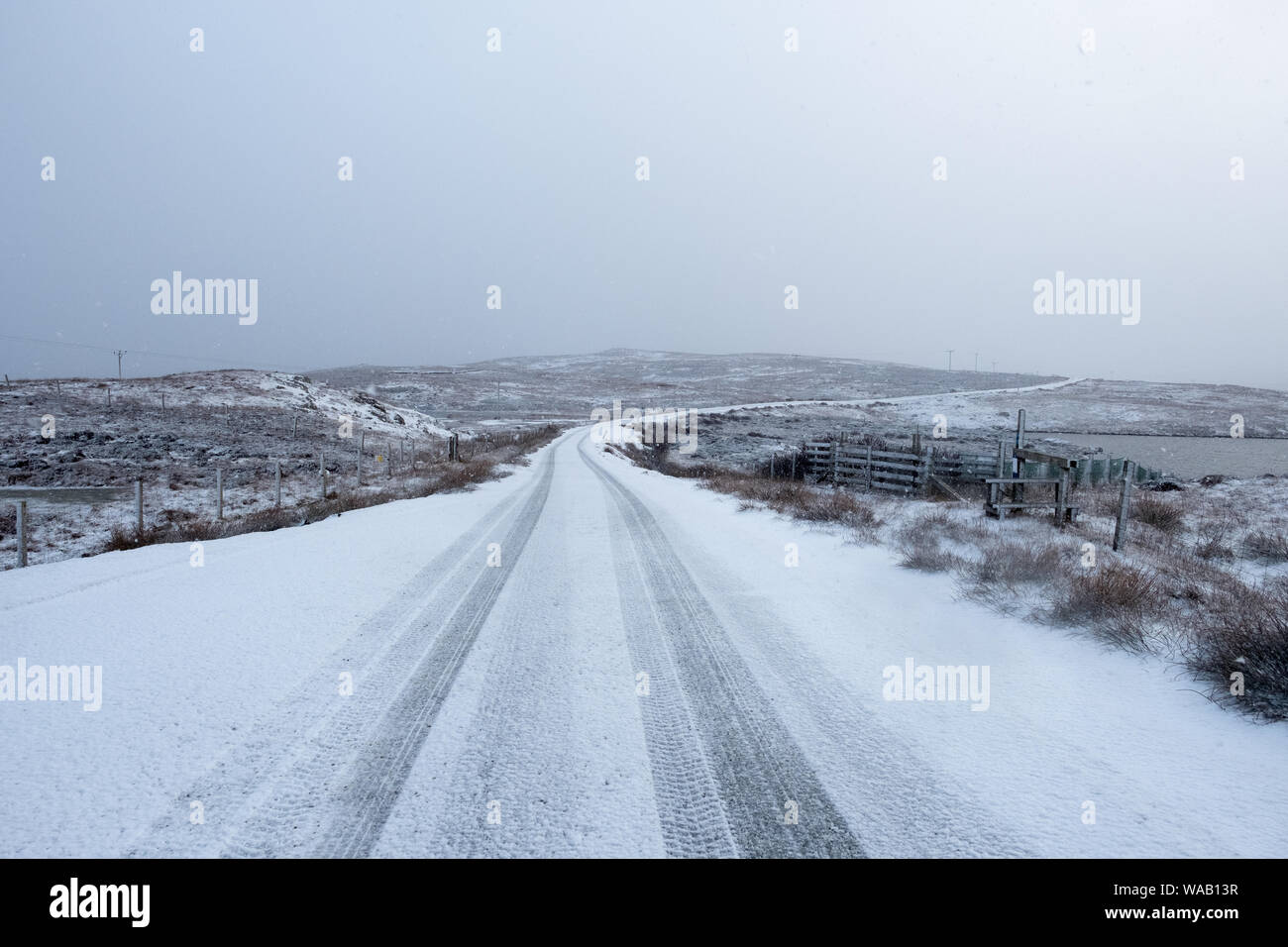 A snowy road in a rural setting with faint tyre tracks and a grey backdrop with room for copy Stock Photo
