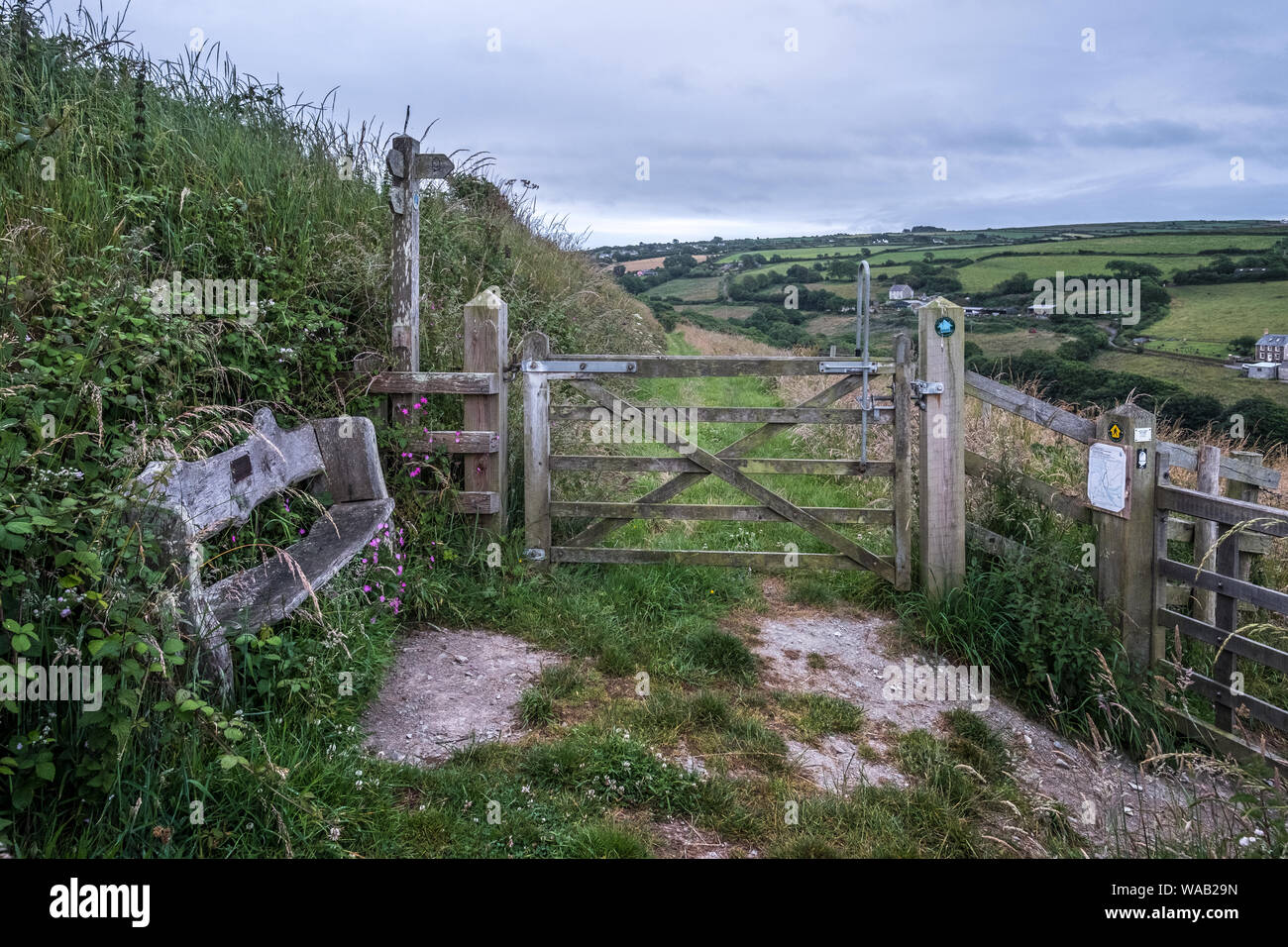 A bench, gate and signs with lush green countryside views on the Pembrokeshire Coast Path, Wales Stock Photo