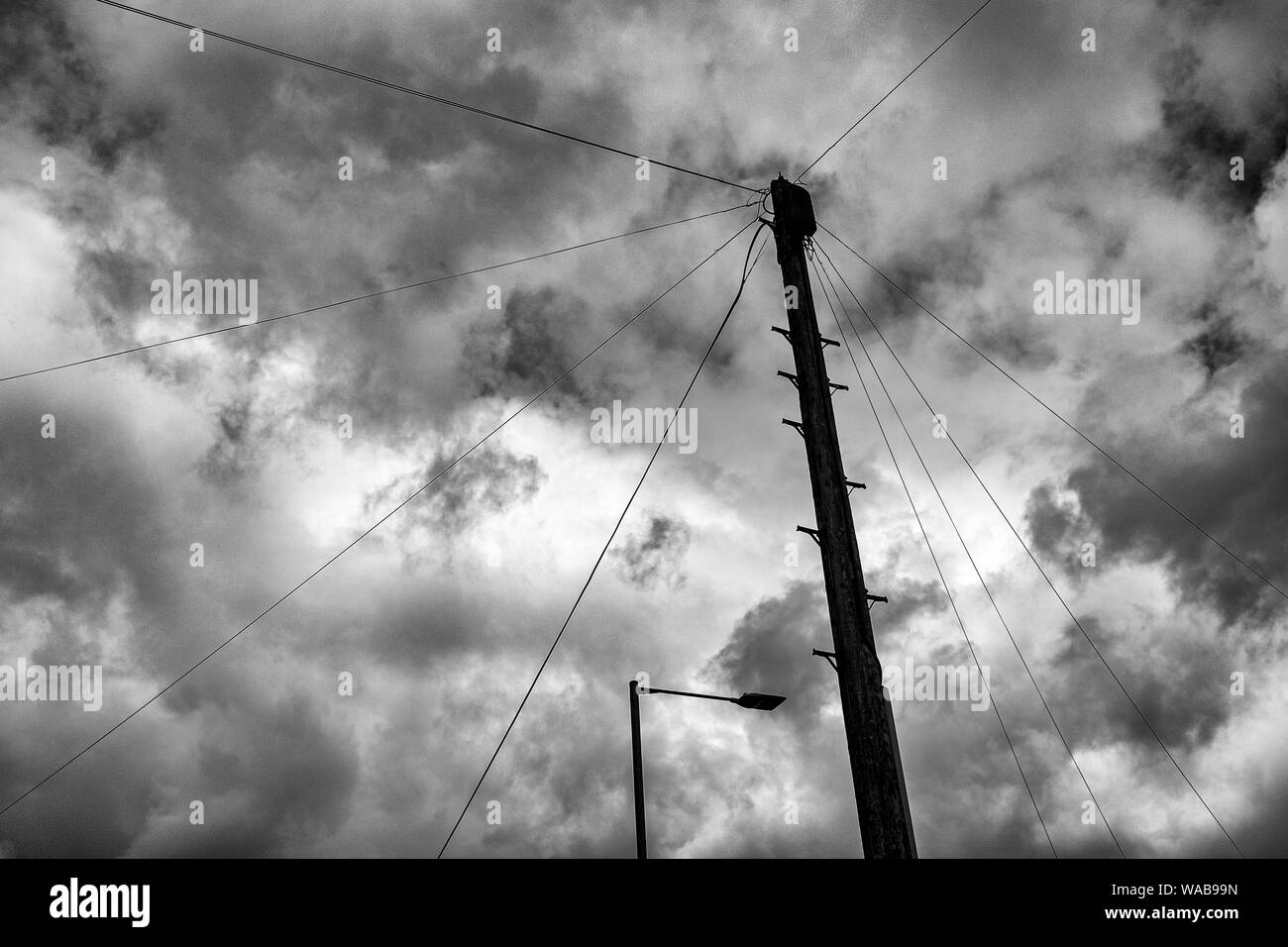 B&W wooden telegraph pole with street light and overcast sky UK Stock Photo