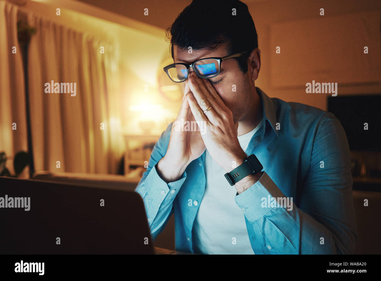 Man sitting in his room working late at night feeling very tired Stock Photo