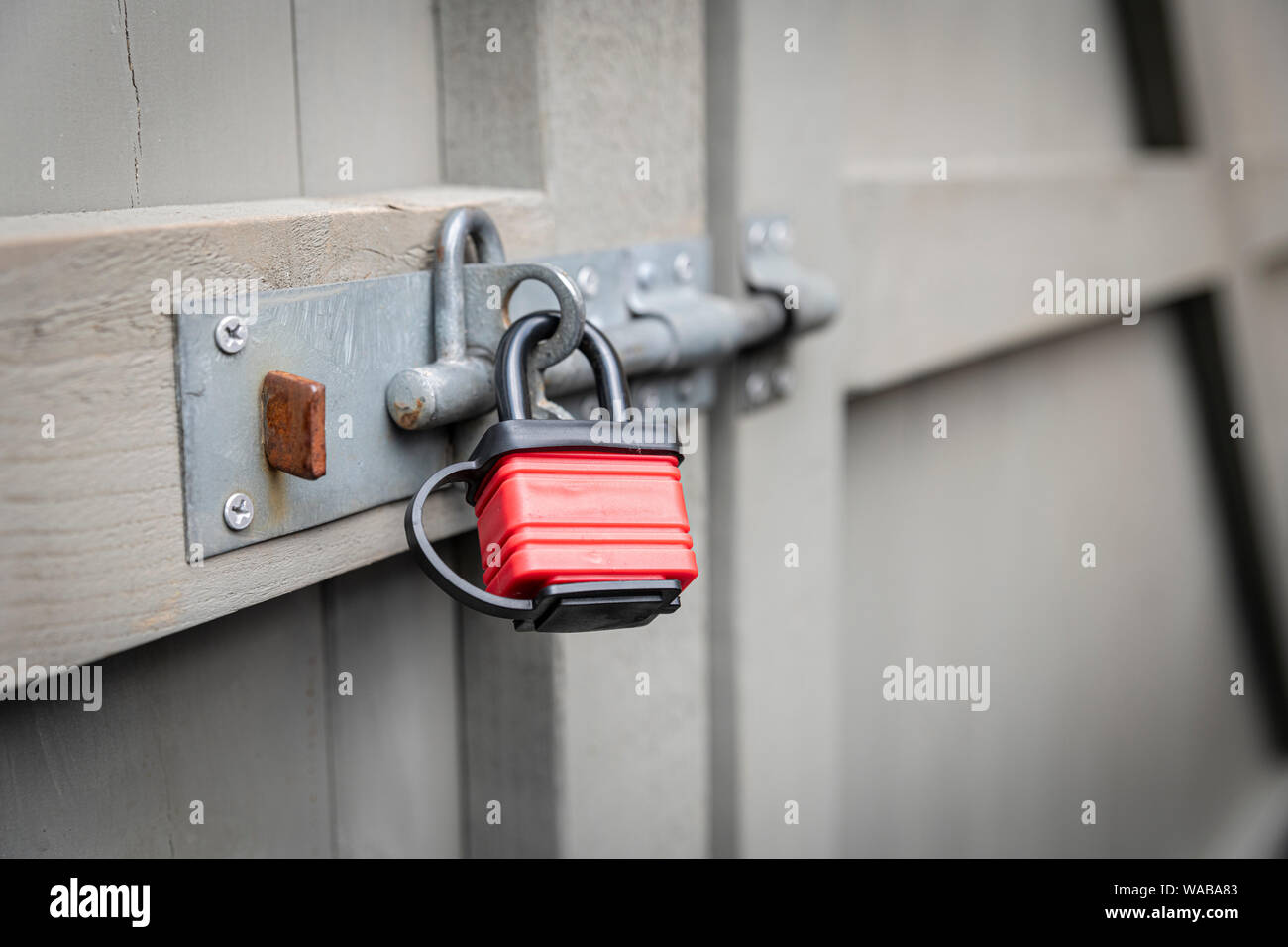 A red padlock securing a bolt on a grey garden gate. Stock Photo