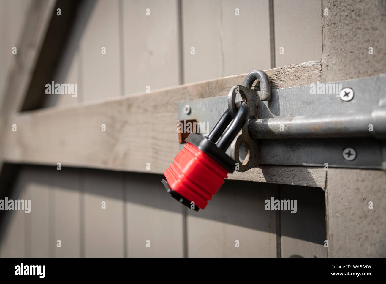 A red padlock securing a bolt on a grey garden gate. Stock Photo