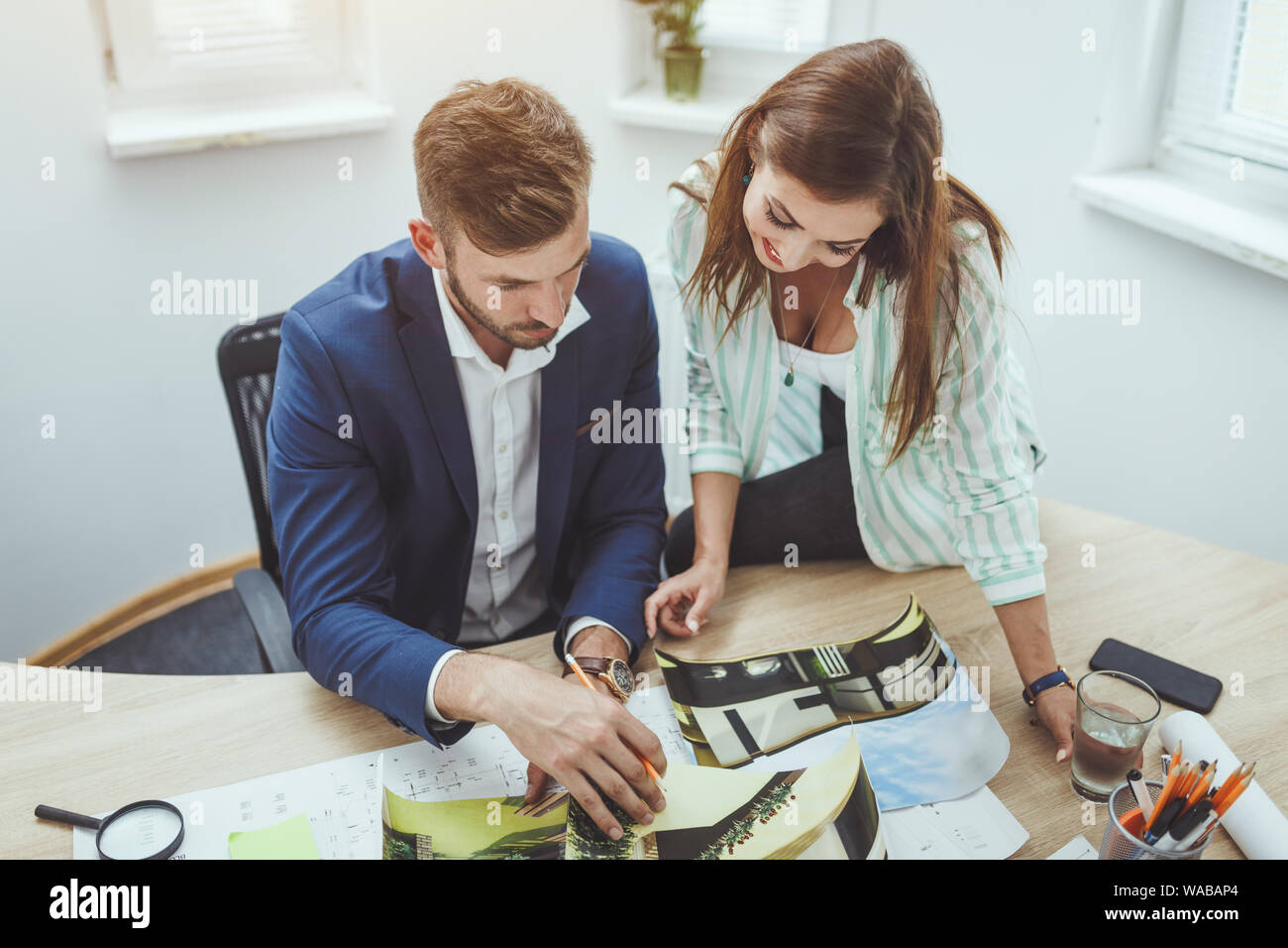 Two young architects working on a new project and communicating while analyzing blueprints in the office. Stock Photo