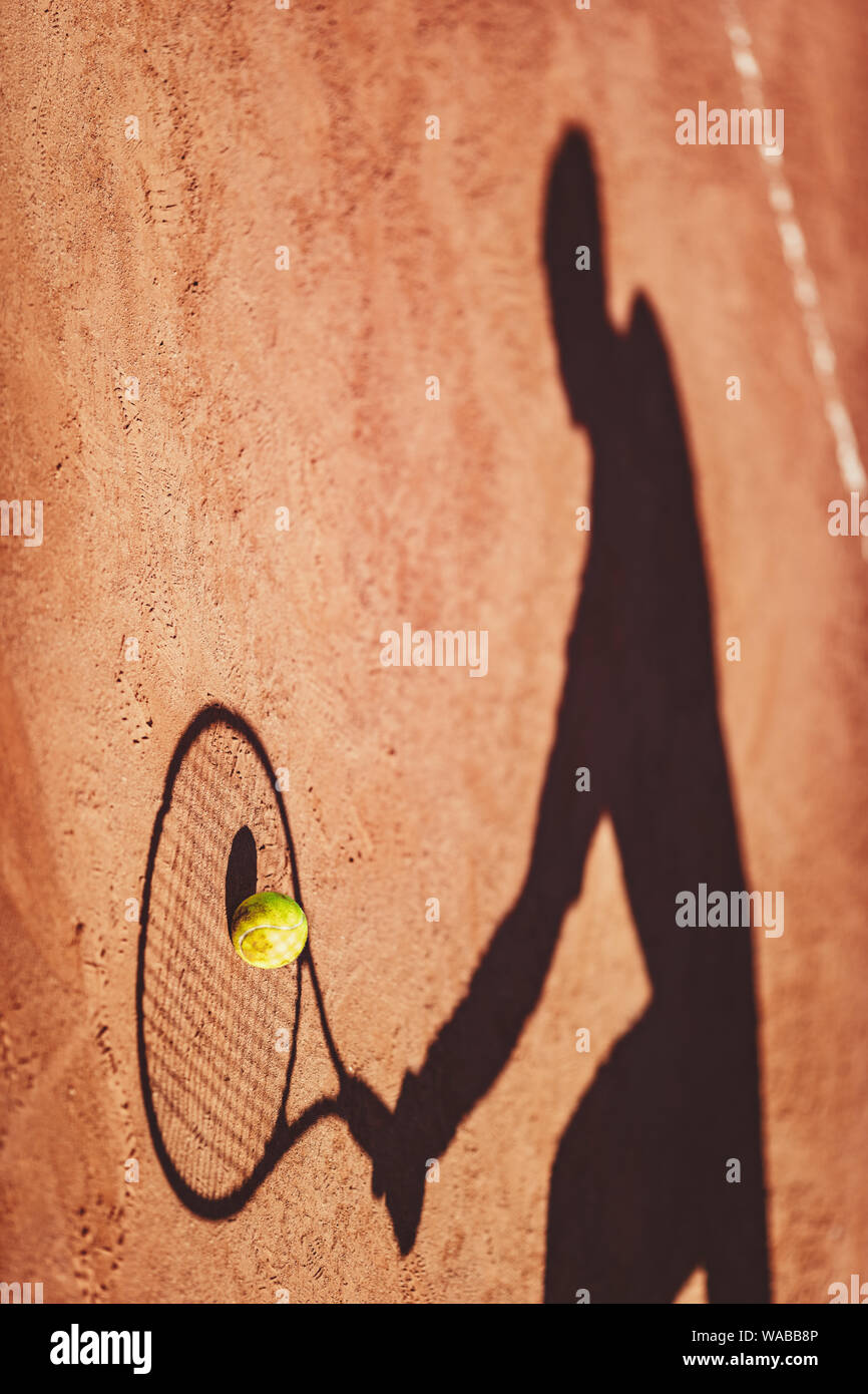 Shadow of a tennis ball and tennis player in action on a clay court . Stock Photo