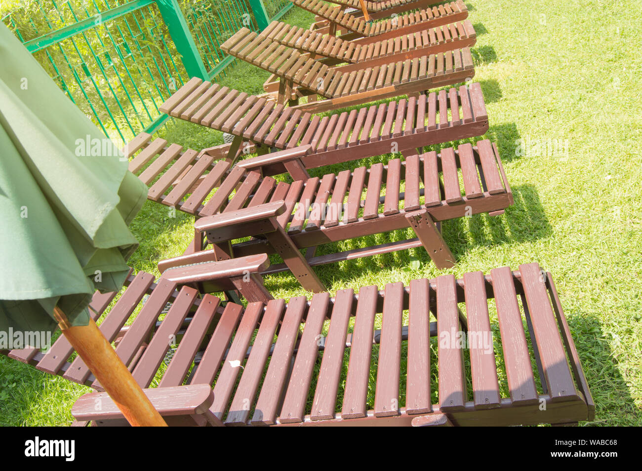 Wooden deck chairs stand in a row on the green grass under the sun in ...
