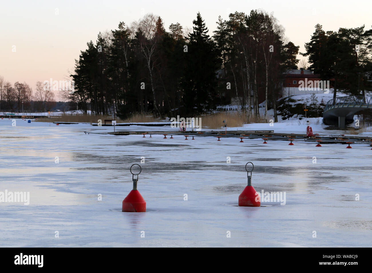 Two red buoys on top of the surface of the frozen Baltic Sea in Espoo, Finland. You can see the partially melting ice and beautiful nature. Stock Photo