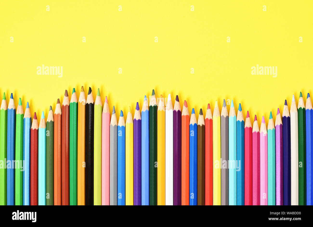Colorful coloring pencils displayed in a wave on yellow background. Stock Photo