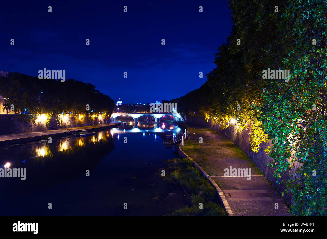 Image of Rione Ponte district. View of white Ponte Umberto I bridge and its reflection, orange trees, waters of Tiber river under dark blue night autu Stock Photo