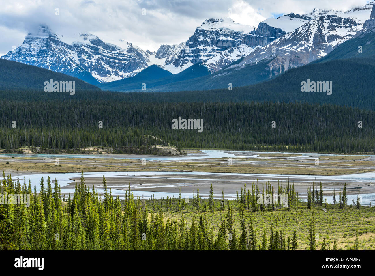 Spring River Valley - Sunlight shining through storm clouds into North Saskatchewan River valley at base of snow-capped peaks, Banff National Park. Stock Photo