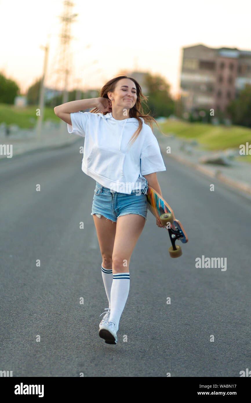 Street portrait of a girl in casual clothes and longboard in her hand  stands on the playground, looks at the camera and poses. Girl model with  ride bo Stock Photo - Alamy