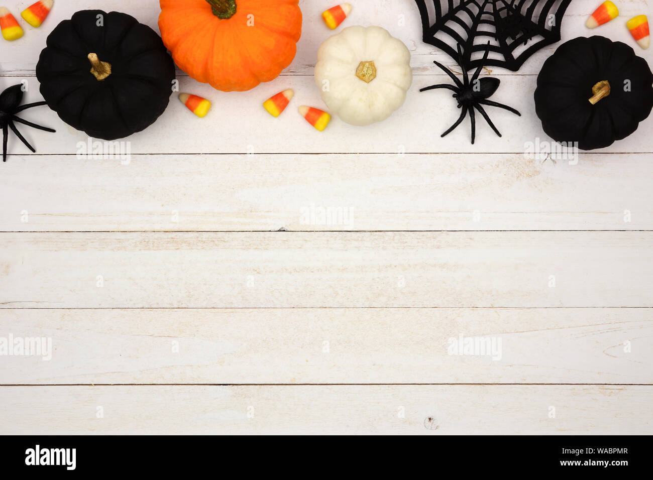 Halloween top border with black, orange and white decor and candy over a white wood background. Top view with copy space. Stock Photo