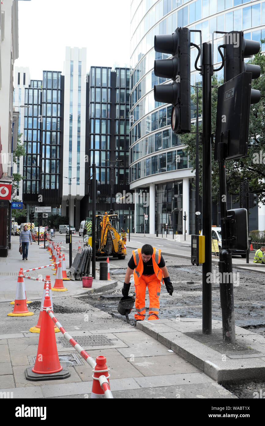 Road repair workers resurfacing street with tarmac at London Wall and Moorgate intersection on a Sunday in the City of London UK  KATHY DEWITT Stock Photo