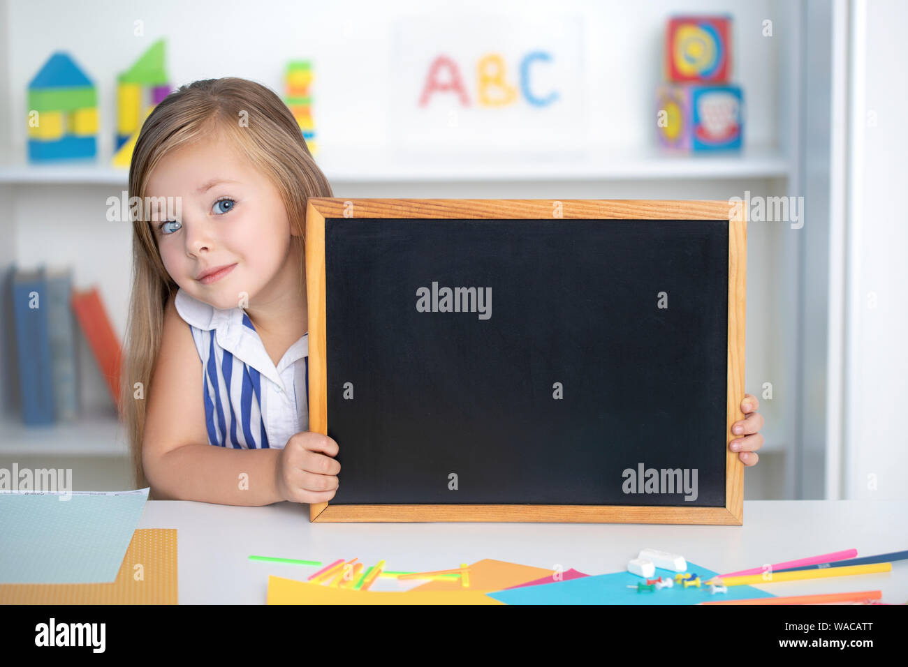 Little cute girl is holding a small empty chalkboard. Mockup Stock Photo