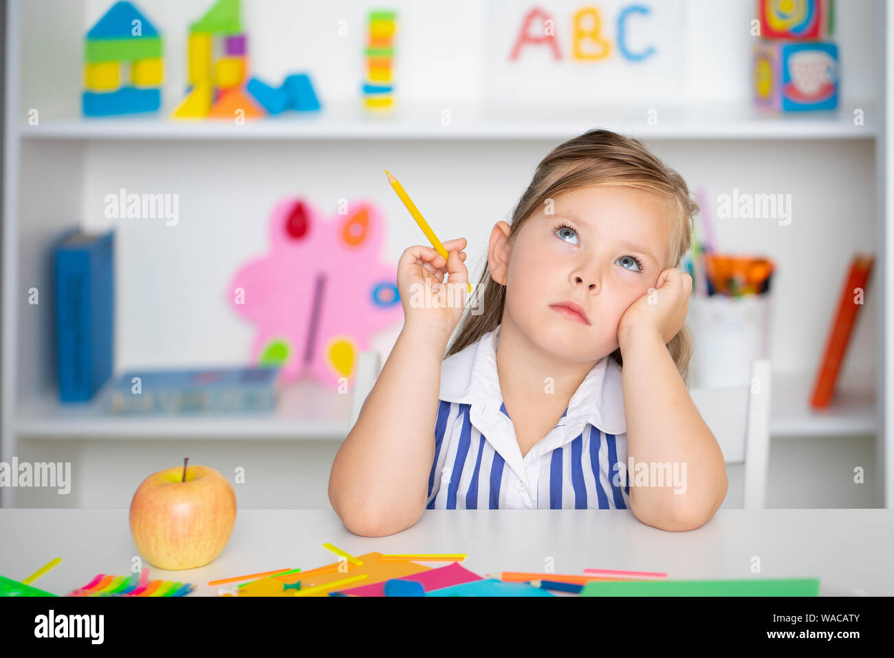 Cute little girl dreams at the table holds a pencil in his hand Stock Photo