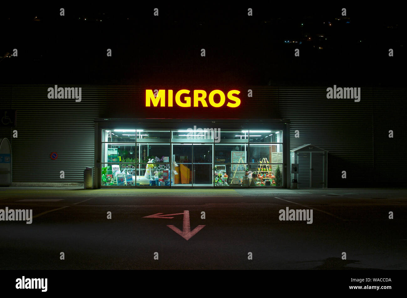 Agno, Ticino, Switzerland - 23rd July 2019 : View of a Migros Supermarket entrance at night. Migros is the biggest retail and wholesale company in Swi Stock Photo