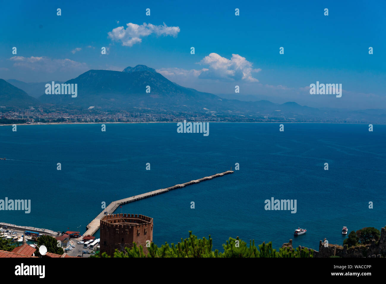 Red Alan Tower on the Mediterranean coast in flowering flora and paths for tourists Alanya, Turkey beautiful background for postcard, booklet Stock Photo