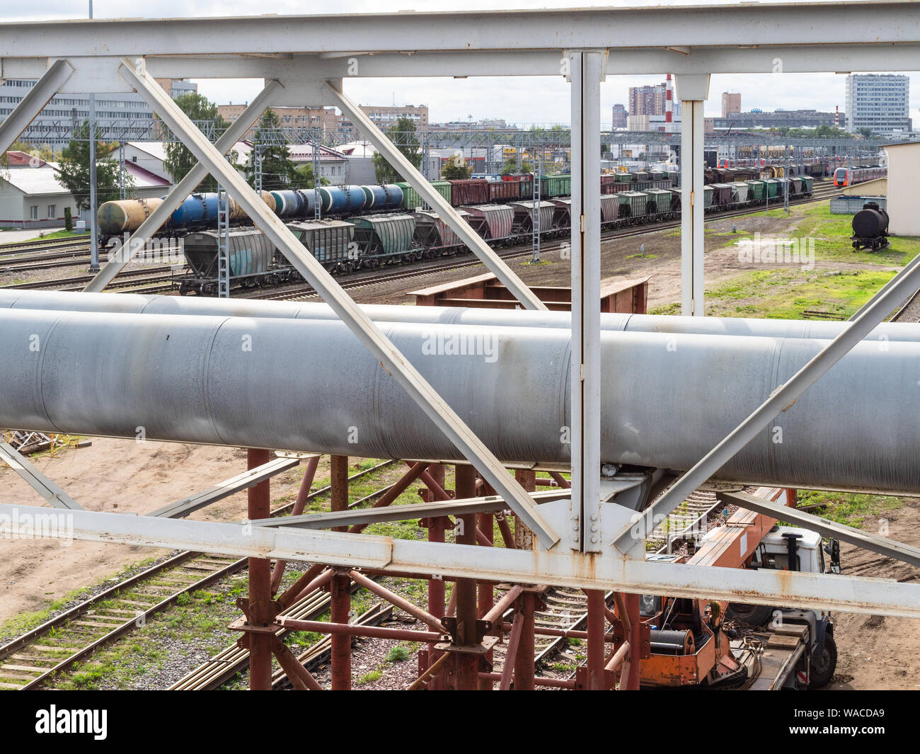 urban landscape - pipeline through railways and two trains on railroad ...