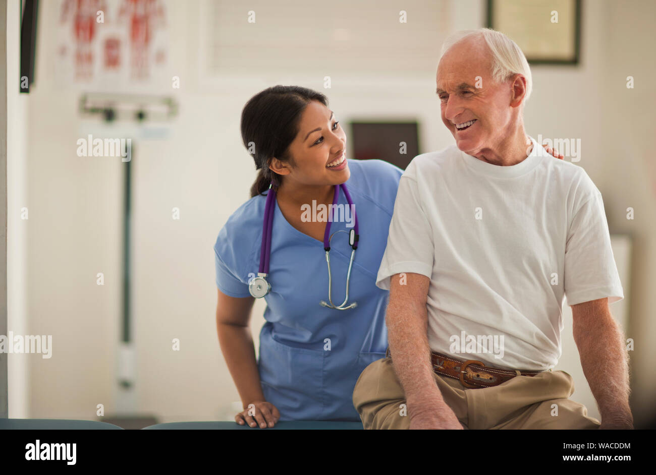 Smiling female nurse comforting an elderly male patient inside an exam room. Stock Photo