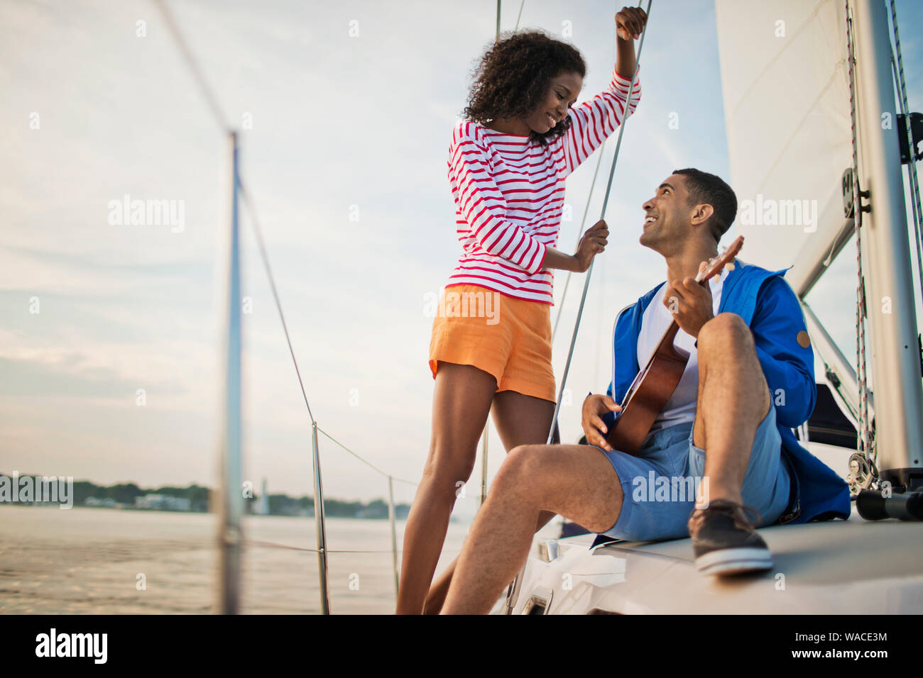 Happy young couple having fun playing the ukulele while sailing. Stock Photo