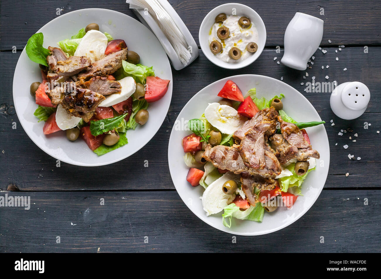 Two servings of grilled meat and salad with vegetables, mozzarella and herbs. Traditional Mediterranean Cuisine Stock Photo