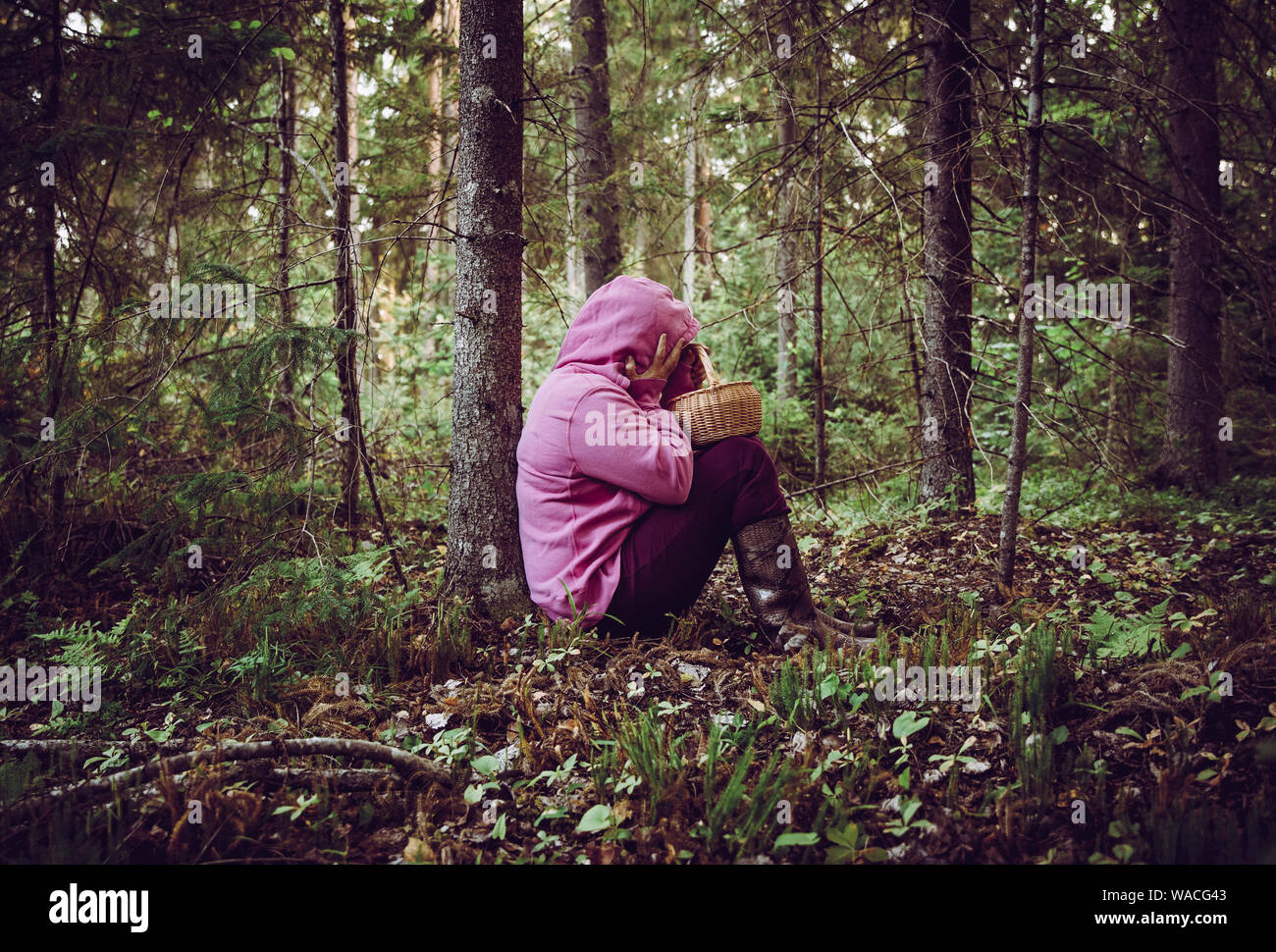Confused person went to mushroom picking and got lost in the forest, disoriented scared and confused, northern Europe, sit under tree. Person lost in Stock Photo