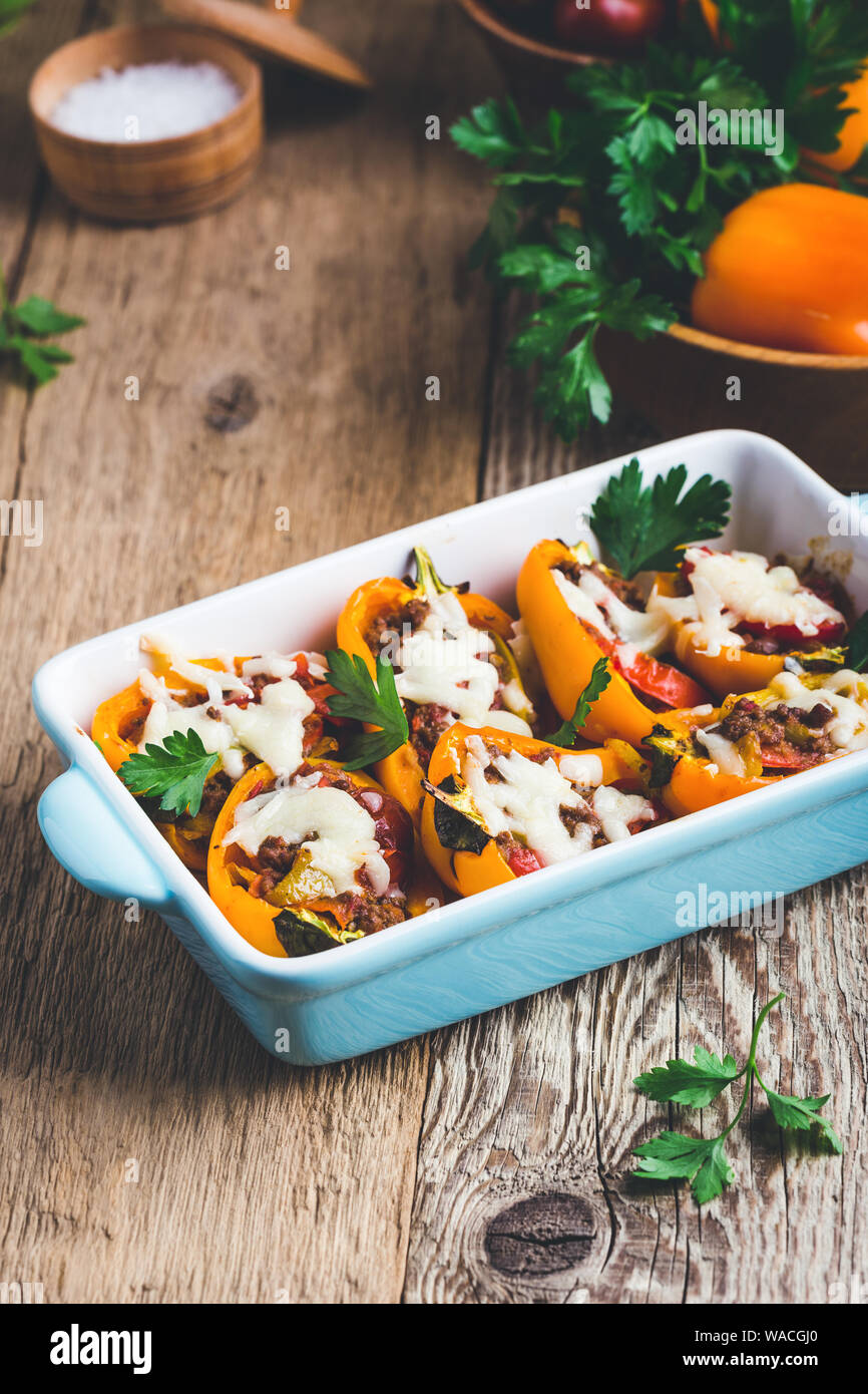 Stuffed orange bell peppers with minced meat and mozzarella cheese in ceramic dish on rustic wooden table Stock Photo