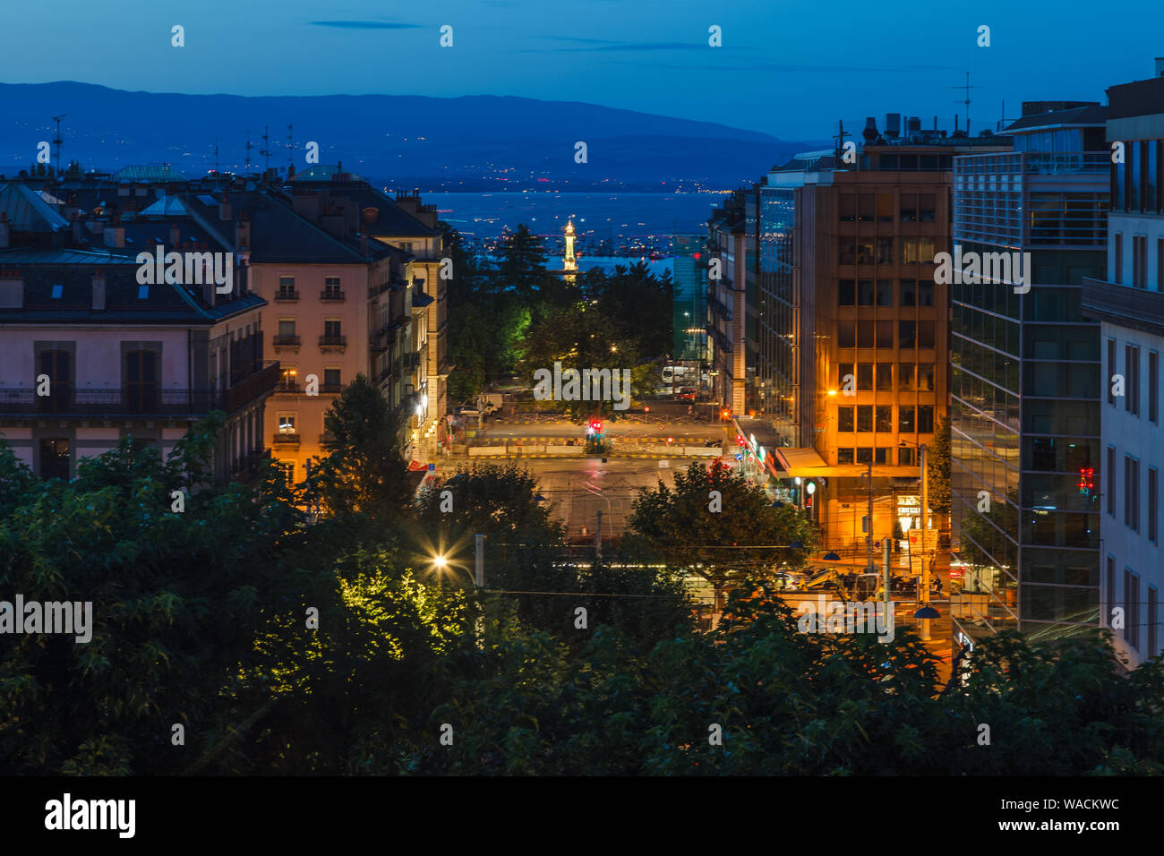 Dusk view of Geneva city streets with buildings, Geneva Lake (Lac Leman) and lighthouse during beautiful summer night, Geneva, Switzerland, Europe Stock Photo