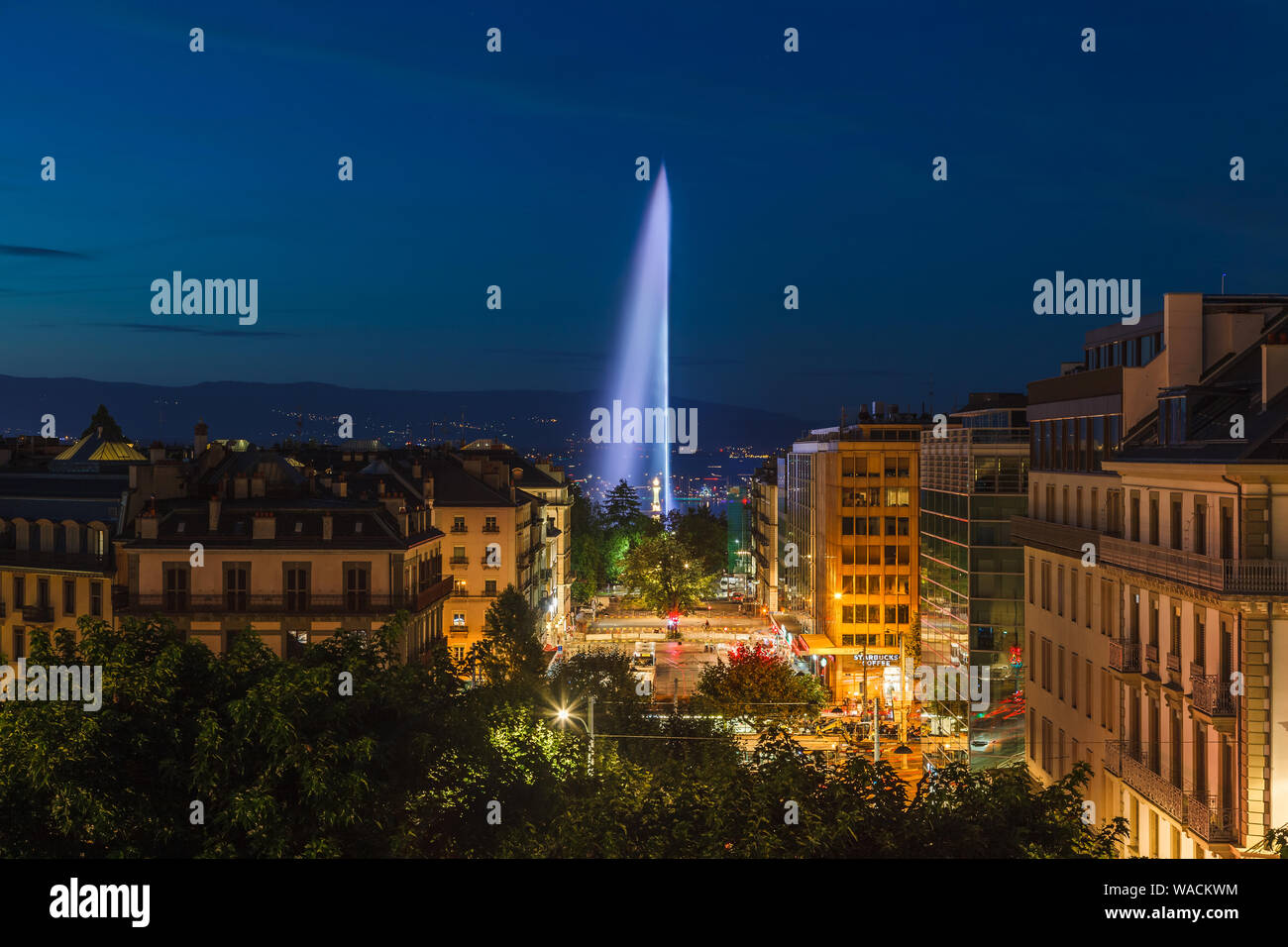 Beautiful panorama view of illuminated Geneva Water Fountain (Jet d'Eau) - the city's most famous landmark, at dusk with blue sky, Geneva, Switzerland Stock Photo