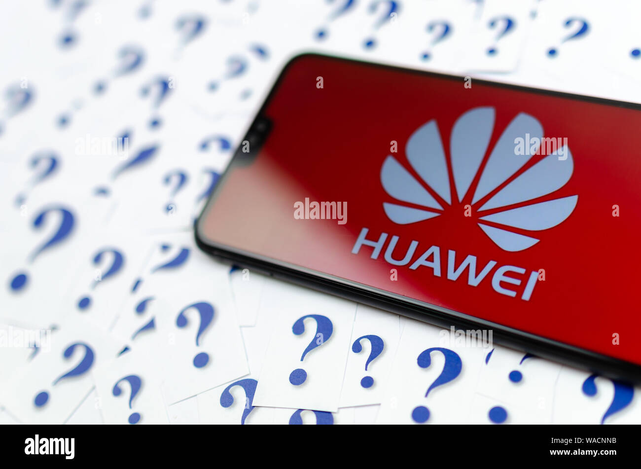 HUAWEI logo on the HUAWEI smartphone and a lot of paper question marks around. The conceptual photo about future of the tech giant in the US. Stock Photo