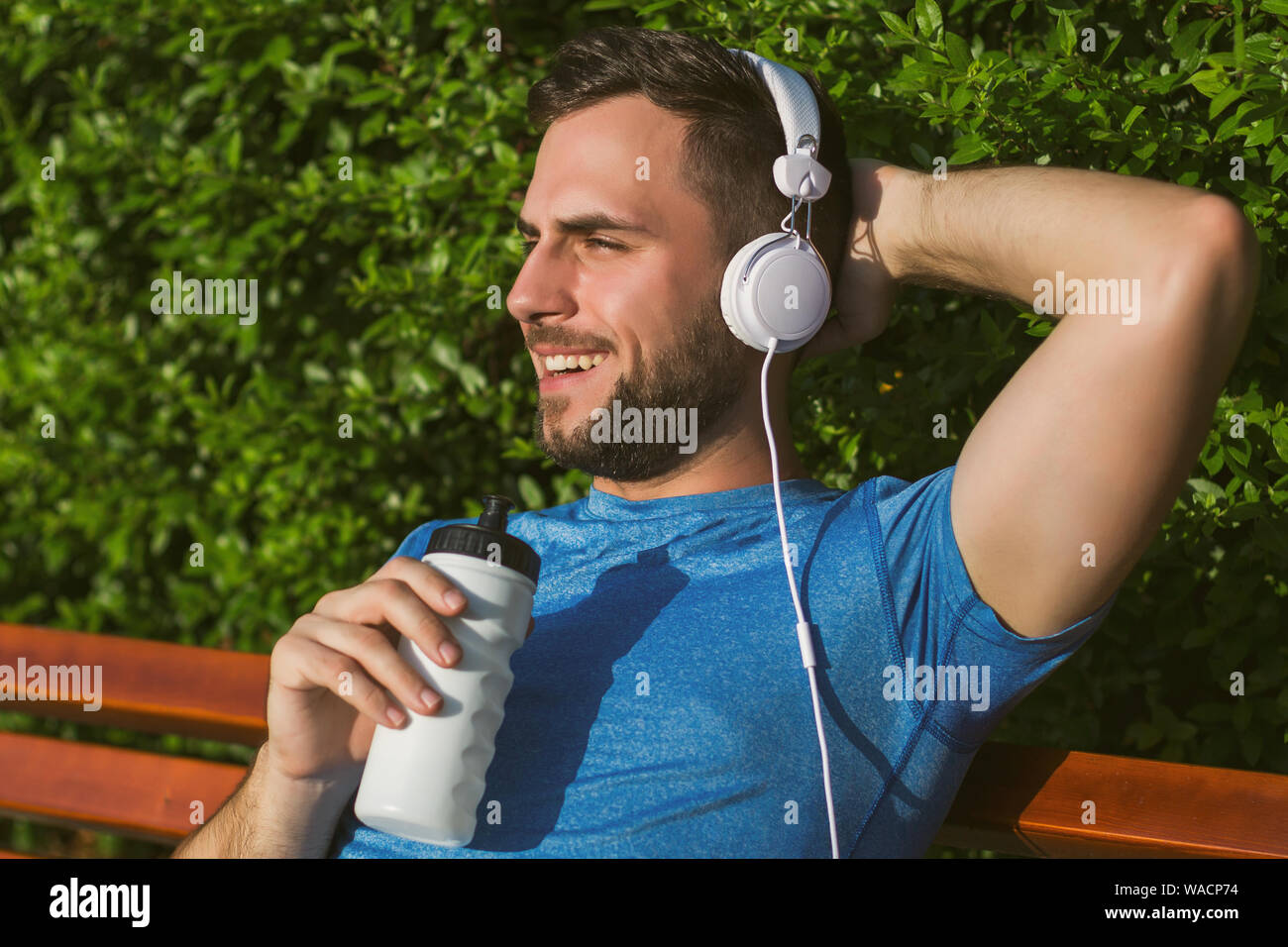 Handsome man with headphones drinking water and resting after exercise in the park. Stock Photo