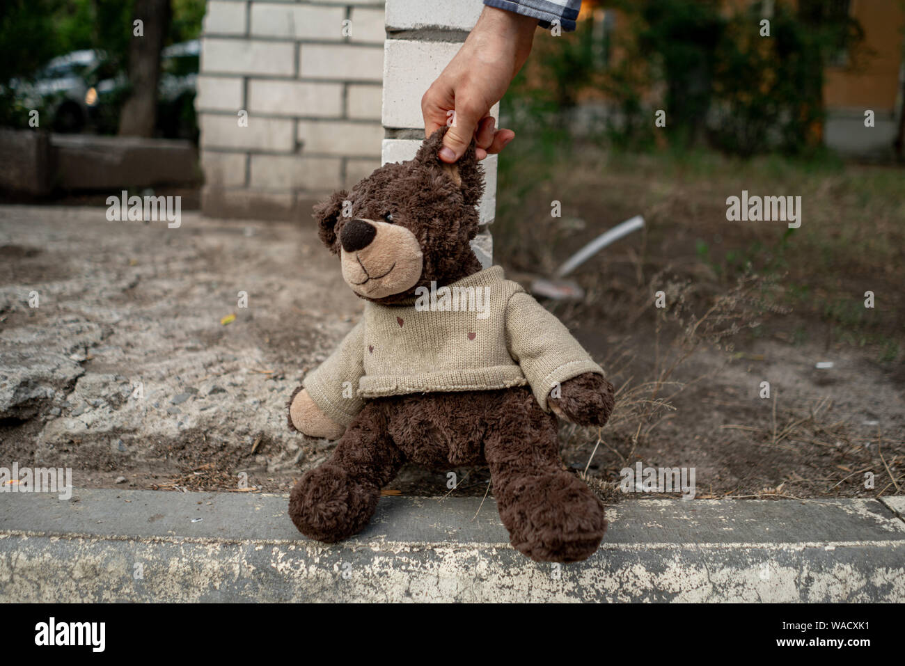 human hand grab the dirty teddy bear from the ground outdoors, lost concept Stock Photo