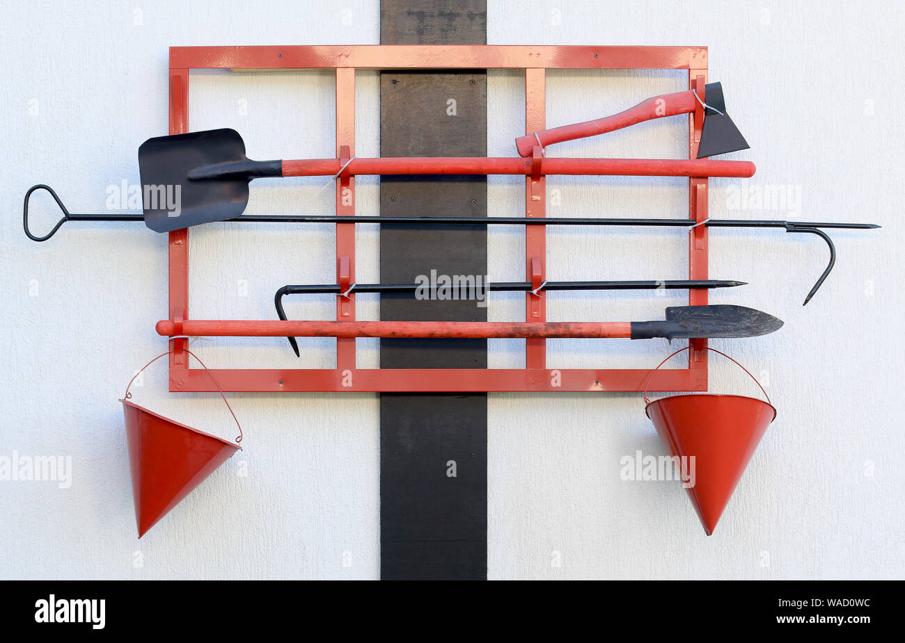 Wall-mounted fire shield open view. Fire extinguishing items. Tools. Shovel, hook, cone bucket, axe and other equipment hanged on fire point. Front Stock Photo