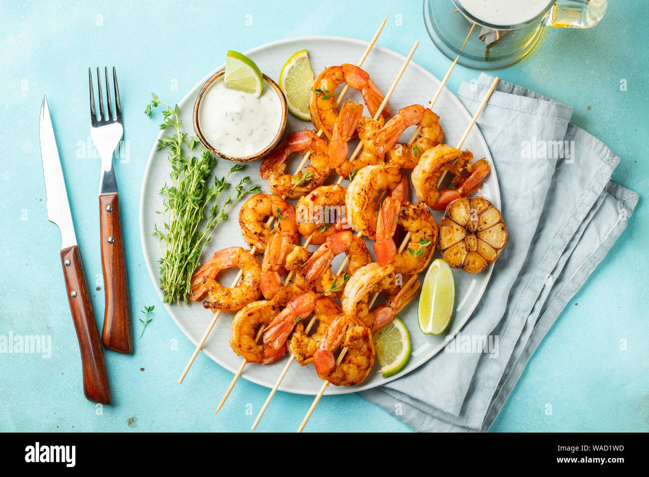 Grilled shrimp skewers or langoustines served with lime, garlic and sauce on a light blue concrete background. Seafood and beer. Top view. Flat lay Stock Photo