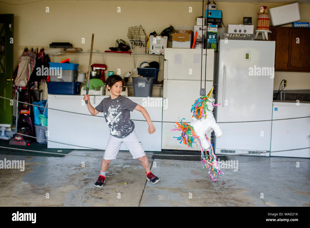 A smiling boy swings a stick at a birthday pinata Stock Photo