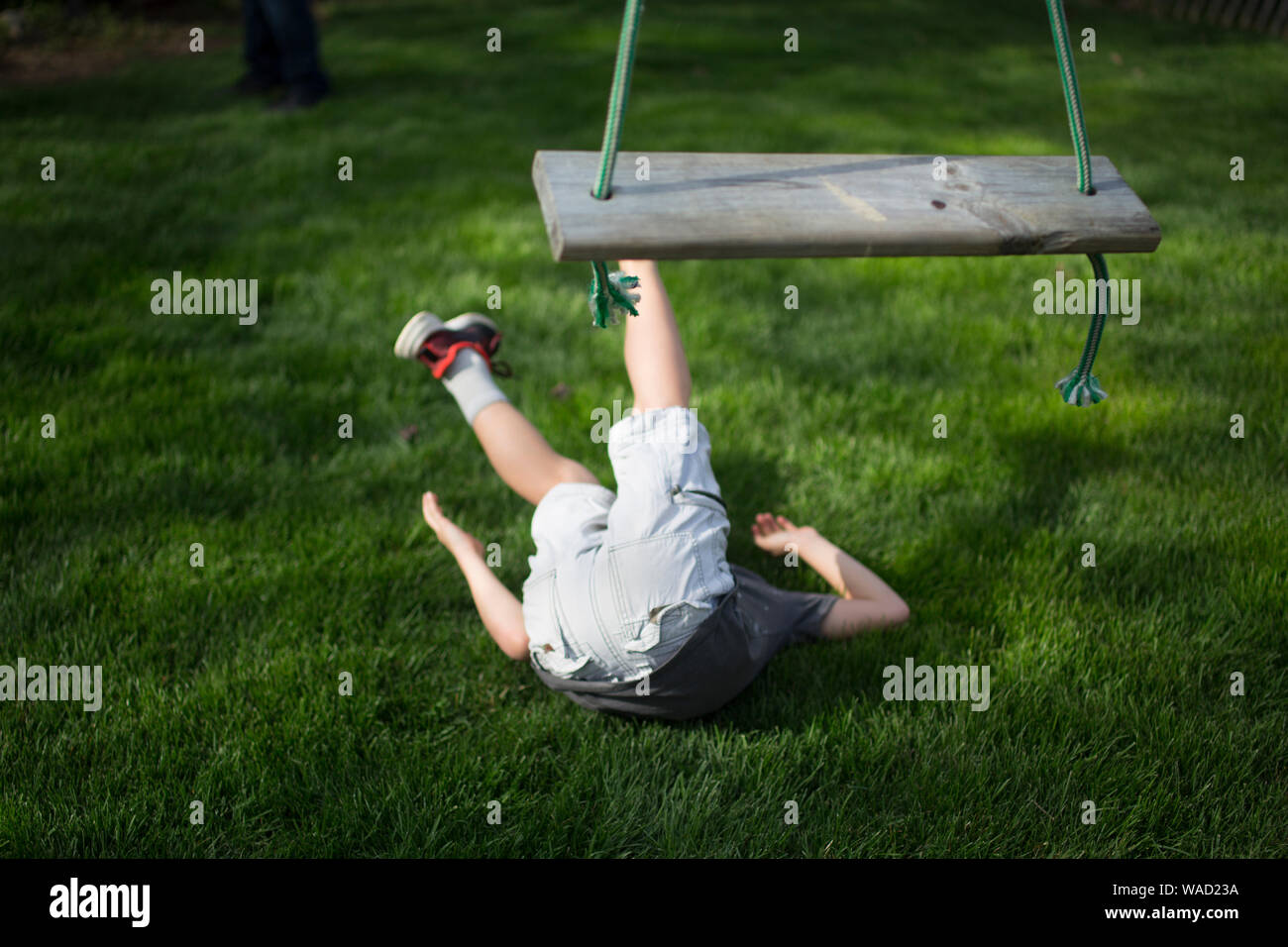 A child lays on the ground after falling from a wooden swing Stock Photo